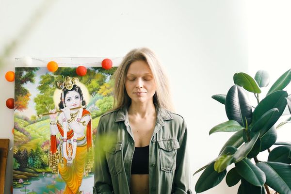 Person meditatively sitting in a sunlit room with plants.